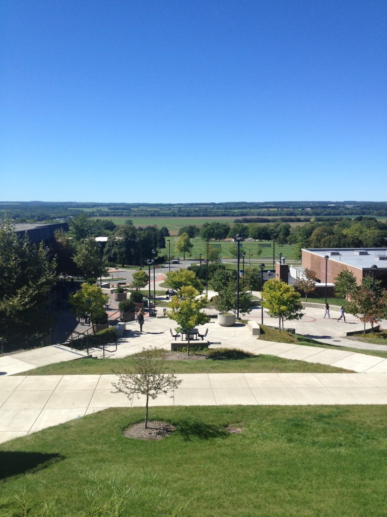A view of the Genesee Valley from the campus of SUNY Geneseo. This photo was taken in September 2013. It is a sunny day. The sky is deep blue, and the valley is green and vast.